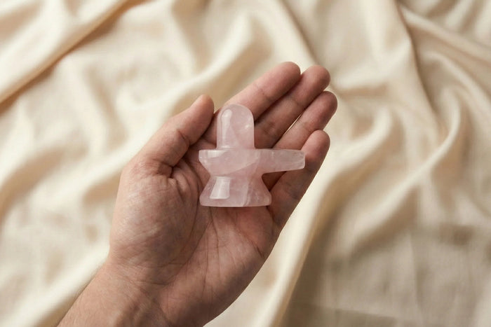 Hand holding a rose quartz crystal on a beige fabric background
