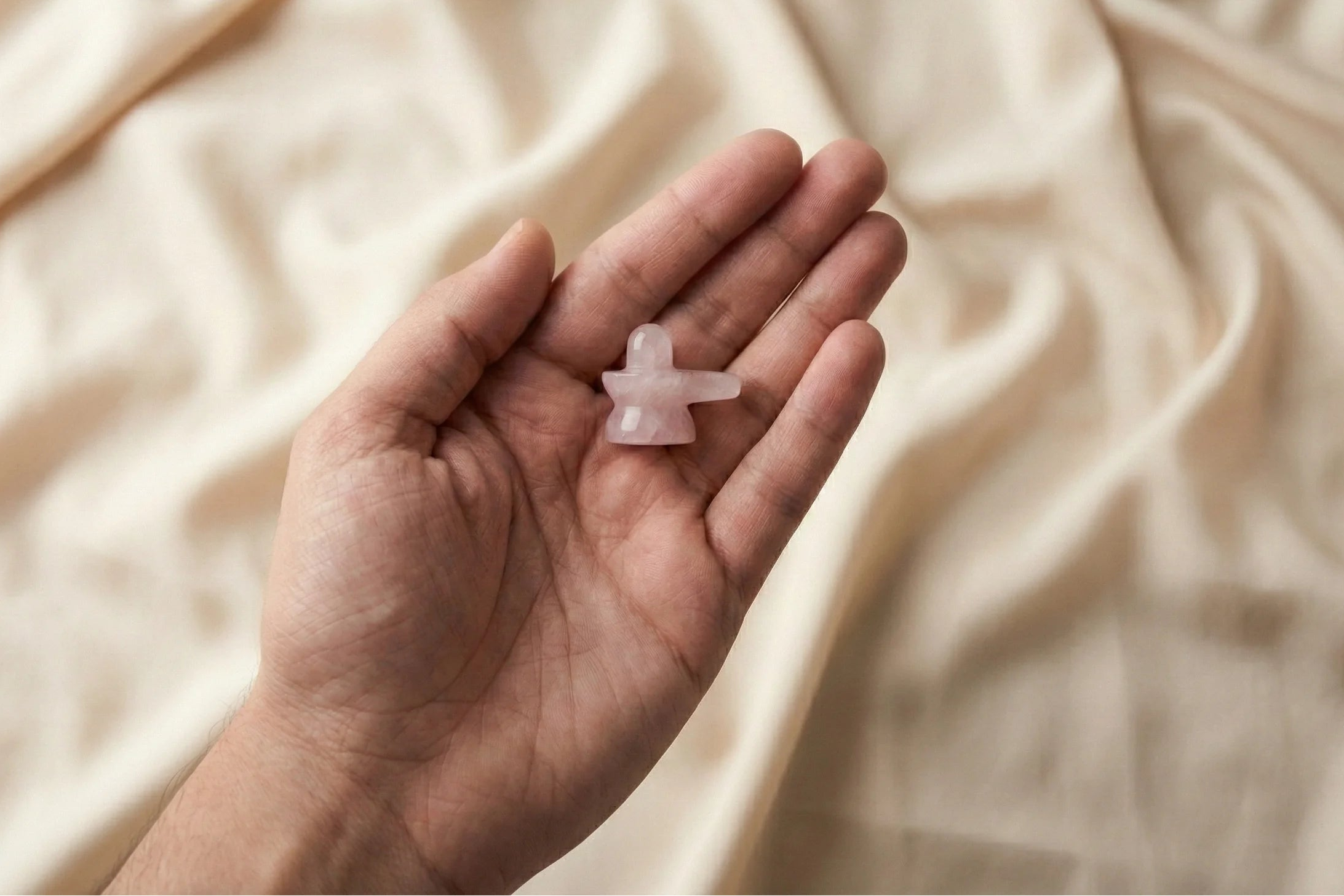 Hand holding a small pink crystal against a beige fabric background