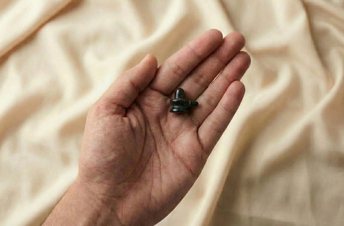 Hand holding Black Tourmaline Shivling (1x1 Inch) against a beige fabric background